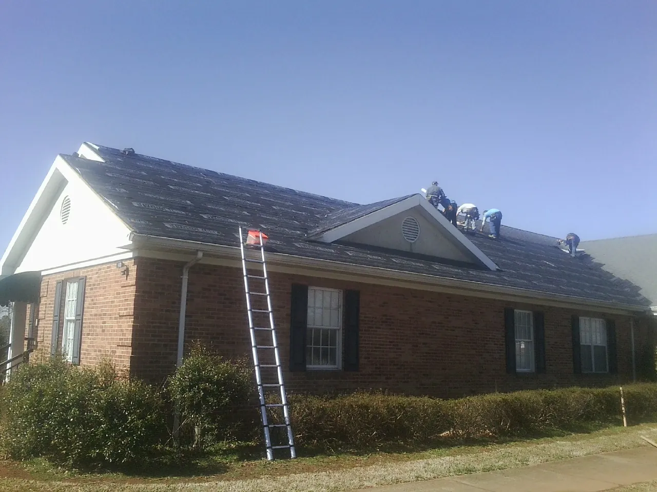 Crew tearing shingles off a brick ranch roof with a ladder set — Metal Roof Repair work by our crew in Mount Morris