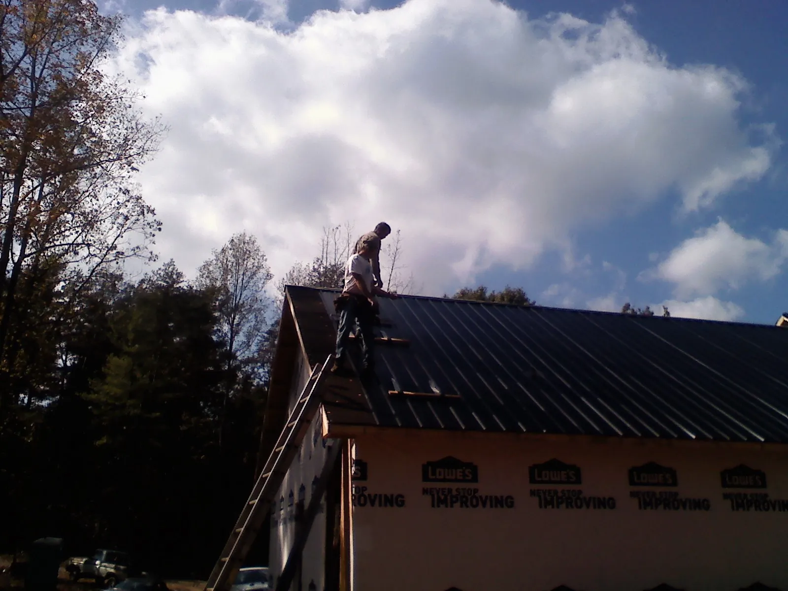 Roofer fastening dark metal panels high against a cloudy sky, from a Roof Inspection job in Mount Morris